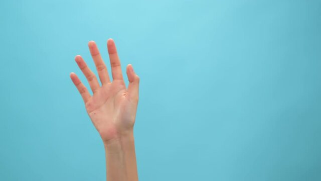 Close up of woman hand showing waving bye on the blue background.