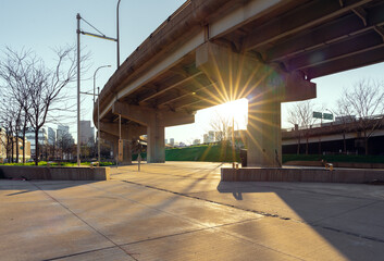 The evening sun dips underneath a road viaduct at an urban park