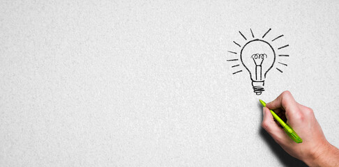 hand with pen drawing a lightbulb symbol on paper background