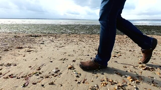 Man walking on pebble and sand beach in jeans and crocs on UK coast