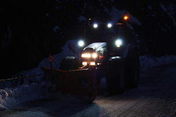 snowplow passes through the snowy mountain streets in the evening to clean up the road traffic