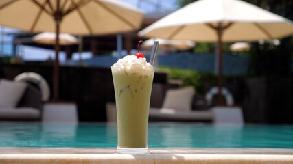 Closeup of iced matcha green tea cocktail with whipped cream and a cherry on top staying on the...