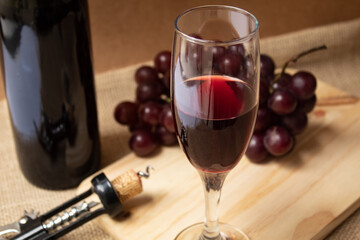 Wine glass with bunch of grapes and bottle of wine in the background