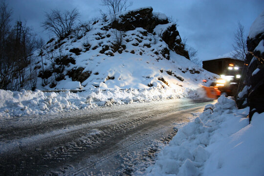 snowplow passes through the snowy mountain streets in the evening to clean up the road traffic
