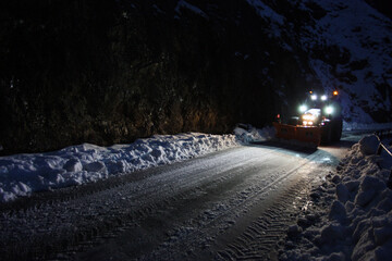 snowplow passes through the snowy mountain streets in the evening to clean up the road traffic