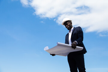african american businessman  in protective safety hard hat looking at blueprint plans on construction site.
