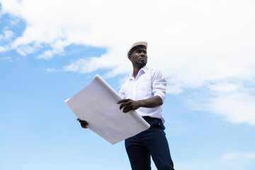 african american businessman  in protective safety hard hat looking at blueprint plans on construction site.