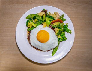 Cooked brown rice with fried vegetables and fried egg in white plate.