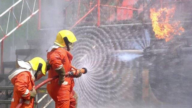 Brave firefighter teamwork fighting a fire on danger rescue duty. Three fireman in fire protection suit spray water from fire hose extinguishing crackle fire flames inside burning leaked gas pipeline.