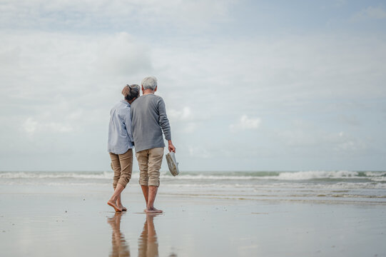 Senior couple holding hands and walking on the beach,other hand of the two was holding a pair of shoes.Plan life insurance at retirement concept.