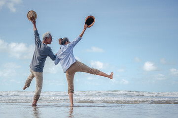 Senior couple jumping in hand in hand on the beach at sunny day, plan life insurance with the...
