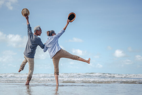 Senior Couple Jumping In Hand In Hand On The Beach At Sunny Day, Plan Life Insurance With The Concept Of Happy Retirement.