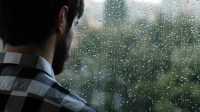 solitude, depression - young sad man looks out the window in a rainy day
