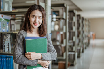 Portrait smiling asian woman standing behind her is a bookshelf in a university library..Education,school,library and knowledge concepts.