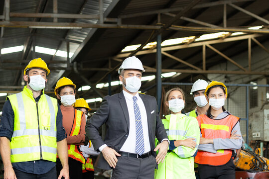 Large group of confident industrial engineer worker and foreman boss with face mask wearing safety equipment standing at manufacturing plant factory.