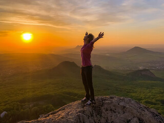 A young woman on the rocks in the mountains at sunset rejoices in life, arms spread apart. Location Beshtau, Pyatigorsk, Russia