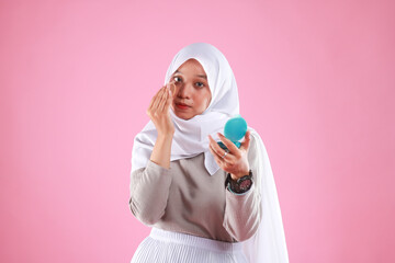 Portrait of beautiful asian woman applying powder puff at cheek makeup of cosmetic isolated on pink background. 