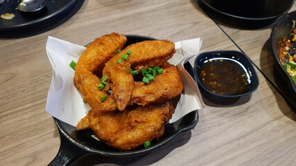 Salted deep fried wing chicken in black hot pan, dish or plate on with sweet or spicy sauce on wooden table at Thai restaurant. Asian food and Delicious crispy meal. 