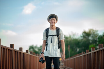 Young male traveler photographer smiling walking on wooden bridge with backpack and holding a camera