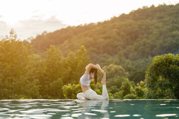Happy Asian woman wearing white sport wear practice yoga king Pigeon pose on the pool above the Mountain peak in the morning in front of beautiful nature views,Feel so comfortable and relax in holiday