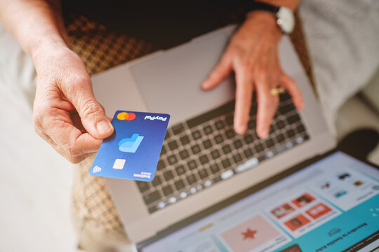 Adult Woman Holding A Paypal Credit Card With Her Hand In Front Of The Computer About To Pay For A Purchase