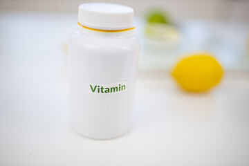 Bottle of vitamins on white table with limes and lemons as background
