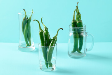 Fresh green chili peppers in a glass on green color background