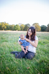 Happy woman sitting on the grass and holding her baby