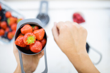 Female hands holding measuring cup full of fresh strawberries