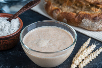 Yeast-free sourdough bread, flour, water and glass jar with dough leaven on the table. Preparing yeast dough for bread