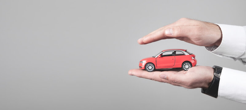 Male hands protect red toy car.