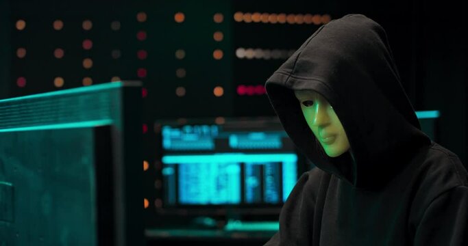 Masked Hacktivist Organizes Massive Data Breach Attack on Corporate Servers. He is in Underground Secret Location Surrounded by Displays