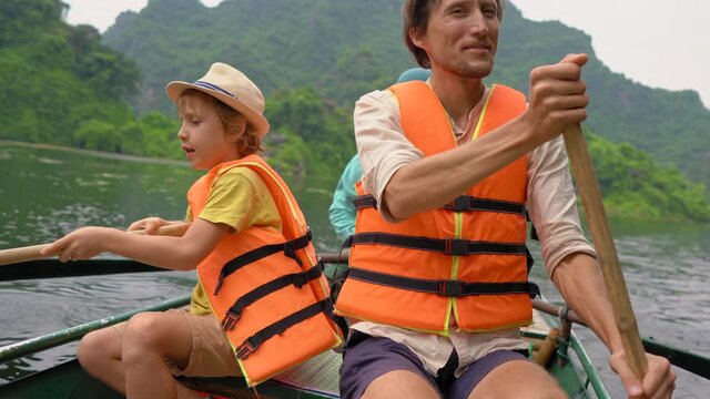 A young man and his son on a boat rowing together on a river trip among spectacular limestone rocks in Ninh Binh, a tourist destination in northern Vietnam. Travel to Vietnam concept