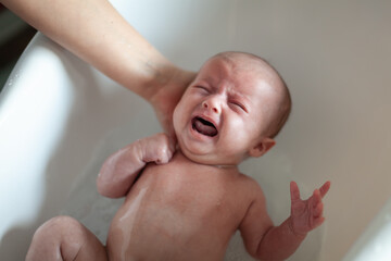 Newborn baby is being bathed by his mother. Newborn baby crying in bath time
