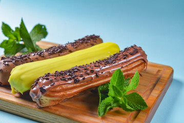 Different coloured eclairs on a wooden board over blue background. French dessert concept, French...