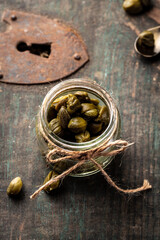 Capers Marinated capers in a jar on dark background. Delicious ingredients for cooking Mediterranean, Italian, Spanish, French cuisine. Pickled, Canned capers. vertical image