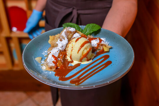 Waiter serving ice cream dessert in restaurant or diner. Eating out concept. Apple pie with ice cream and caramel sauce.