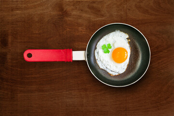 Small empty black frying pan with red plastic handle with fried chicken egg, scrambled eggs on brown natural wooden table, rustic style