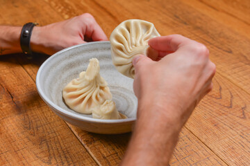 Man eats khinkali - Georgian dumpling served in a white bowl over rustic wooden table. Eating, still life.
