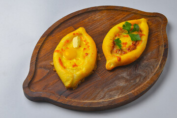 Khachapuri with cheese and egg on a wooden board over white background. Georgian cuisine concept.