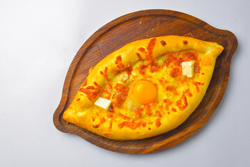 Khachapuri with cheese and egg on a wooden board over white background. Georgian cuisine concept.