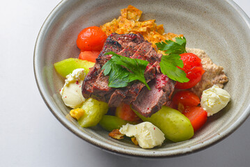 Juicy steak cut and served in a bowl with cut vegetables and feta cheese. Delicious Georgian dish.
