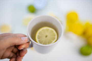 Female hand holding a cup of lemon tea above limes and lemons