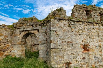 Fototapeta na wymiar Wall of ancient ruins of castle among green grass. Ukrainian architectural landmark.
