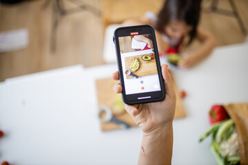 Female hand with a smartphone recording a little girl cutting an avocado