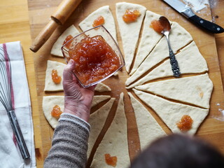 Woman is hands spread jam on a slab of dough to form croissants on a cutting wooden kitchen baking board. Favorite and useful hobby. Home cooking.