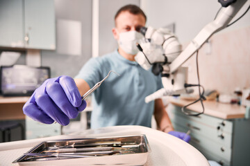Close up of male dentist hand in sterile glove holding metal dental explorer. Stomatologist in...