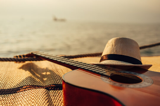 Guitar and hat on reed mat near the sea at sunset. Travel, vocation, holiday, summer concept.