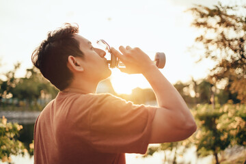 handsome man drinking water on a sunny day after running. Sport, fitness workout concept.