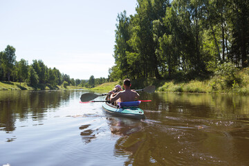 Fototapeta na wymiar A couple of men and women kayak on the river in the summer. Active recreation, family travel, extreme adventure, sports and ecological domestic tourism. Equipment for rafting, boat, oars.